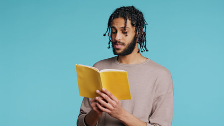Middle Eastern man reading book from publisher aloud, telling story, enjoying hobby. BIPOC person narrating literature novel, doing critique essay, isolated over studio background, camera Bの写真素材