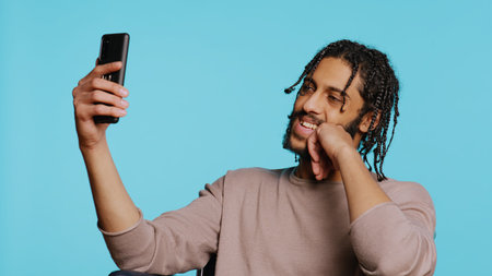 Man in wheelchair saluting friend over online videocall on cellphone, enjoying leisure time. Smiling person with disability bonding with mate using phone videoconference, studio background, camera Bの写真素材