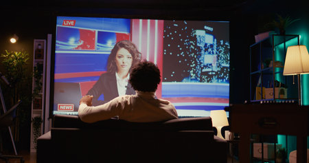 African american man in home theatre watching smart TV channel showing journalist talk about cybercriminals attacks subject. Cord cutter relaxing on couch with VOD subscription based news channelの写真素材