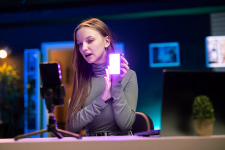 Teenage online show host being sponsored by partnering brand to do mini RGB lights unboxing video. Woman does influencer marketing, presenting viewers led production tool productの写真素材