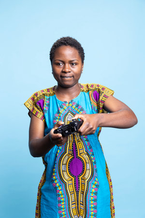 Cheerful young adult playing videogames with a controller, enjoying online e sport championship over blue background. Smiling joyful woman having fun with a gaming tournament on camera.の写真素材