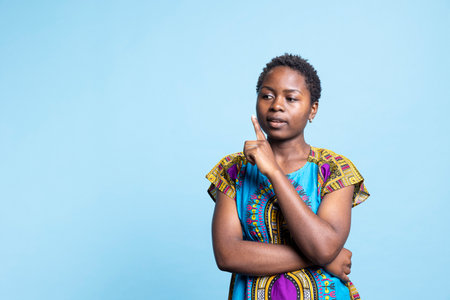 African american gorgeous person trying to find new solutions, being uncertain and contemplating about innovative ideas. Young female model feels unsure, wearing colorful ethnic costume.の写真素材