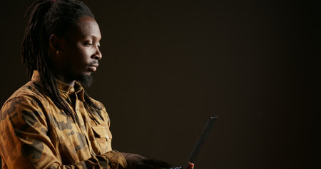 African american guy scrolling through online network pages, looking for something while he uses laptop over black background. Young adult holding wireless pc and searching the websites.の写真素材