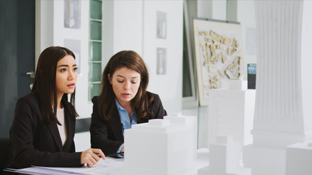 Architectural agency workers taking notes on blueprints, calculating real scale measurements to ensure the perfect elements for the construction team. Women developers studying 3d printed model.の写真素材