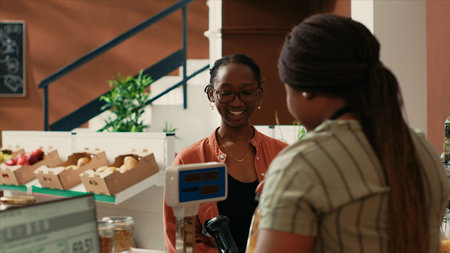 Local vendor weighting bulk products on sale for female buyer, small business owner at neighborhood grocery store. African american woman selling pasta and sauces in reusable glass jars.の写真素材
