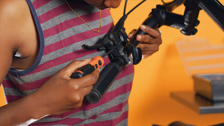 Woman uses screwdriver to make sure brake levers are secure on handlebars in studio background atelier shop. Close up shot of expert mechanic unscrewing bike parts in order to mend themの写真素材