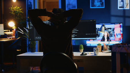 Man doing IT support job from home office, stretching after sitting on desk chair all day. Programmer loosening up, relaxing after typing on computer for long period of time, camera Aの写真素材