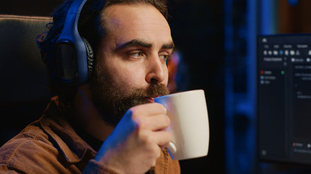Developer listening music and drinking coffee while doing programming during remote job shift in...