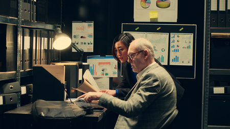 Team members cross reference data to track down potential suspect, using archived records and forensic evidence reports. Officers uncover crucial information to help solve legal case. Camera A.の写真素材