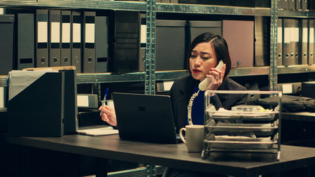 Private detective conducting background check on landline phone call, asking forensic experts about suspects associated with archived cases. Agent searches for relevant information. Camera A.の写真素材