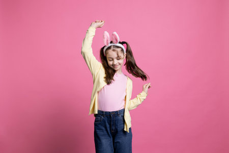 Energetic and positive kid dancing in studio while wearing bunny ears in excitement of Easter Sunday celebrations. Pleased carefree youngster who displays comfort in her dance skills.の写真素材