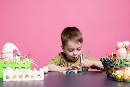 Adorable toddler smiles as he uses watercolors and paints to decorate eggs and centerpieces for the Easter celebration festivity. Little ecstatic young boy exploring creativity with art supplies.の写真素材