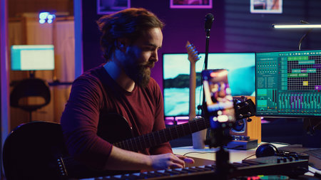 Musical producer doing online guitar lessons with smartphone vlog, recording himself singing and playing acoustics. Artist teaching people how to play and tune instrument with strings. Camera A.の写真素材