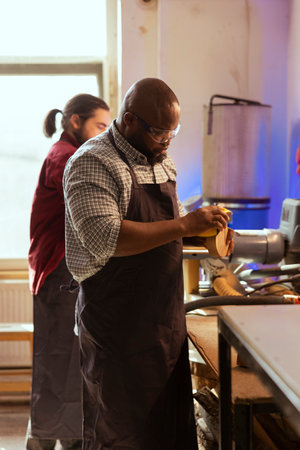 African american artisan in studio using sandpaper for smoothing wooden surface, creating wood art designs. BIPOC person using sanding sheets to refurbish damages suffered by timber blockの写真素材
