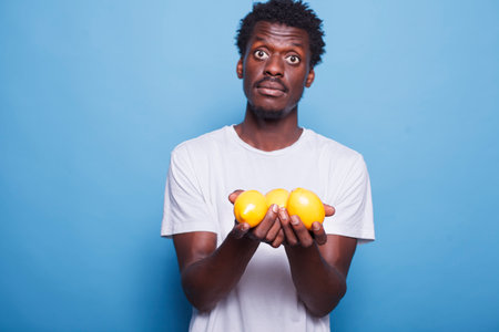 African american male individual carrying lemons and looking at the camera. Black man holding and showing yellow, citrus fruits for vitamins, nutrition, and healthy lifestyle.の写真素材