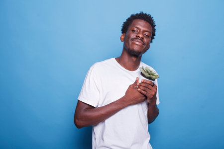 Portrait of black guy carrying container with plants for their botany hobby. Cheerful african american man holding dearly a flowerpot with green leaves for gardening concept and ecology.の写真素材