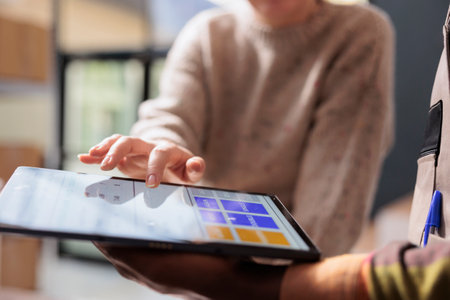 Diverse team analyzing goods quality control report on tablet computer, working at customers orders in storehouse. Stockroom employee preparing packages for delivery, checking clients detalisの写真素材