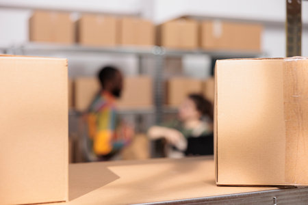 Selective focus of cardboard boxes in warehouse, in background diverse team preparing customers packages for delivery. Storage room employees discussing online orders, checking shipping detalisの写真素材
