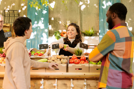 Boyfriend and girlfriend tasting fresh green apple before purchasing organic fruits and vegetables at farmers market. Happy farm produce stand owner offering free samples, bio natural products.の写真素材