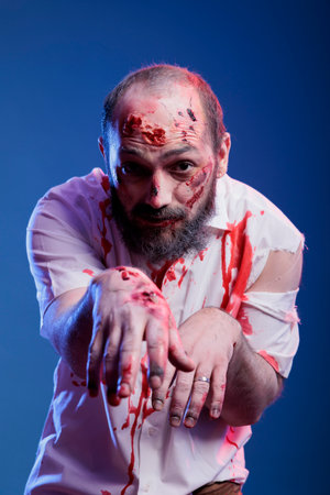 Portrait of man dressed as terrifying creepy zombie covered in blood for halloween party. Person wearing scary makeup, pretending to be undead monster with scars, studio backgroundの写真素材