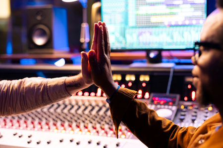 Pleased artist doing high five gesture with sound designer after finishing a song, processing and editing music for his new album. Singer and producer celebrating successful tracks in studio.の写真素材