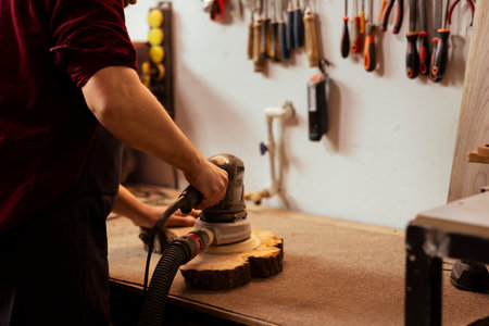 Carpenter using orbital sander with finer sandpaper grits to achieve smoother and more refined finish. Woodworker using angle grinder on wood, achieving professional quality resultsの写真素材