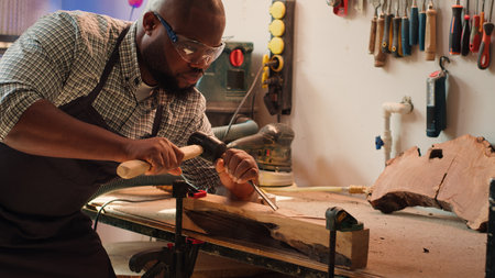 African american sculptor shaping raw timber using chisel and hammer in carpentry shop, creating...