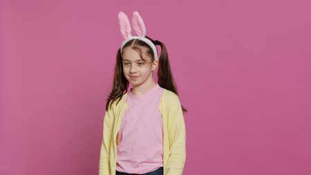 Confident cheery girl showing dance moves in the studio, feeling cheerful and positive about easter holiday festivity. Talented child dancing around and wearing bunny ears. Camera A.の写真素材