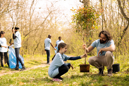 Man and little girl team up and plant a tree together in the woods, preserving the natural environment. People volunteering to help forest ecosystem grow and preserve wildlife.の写真素材