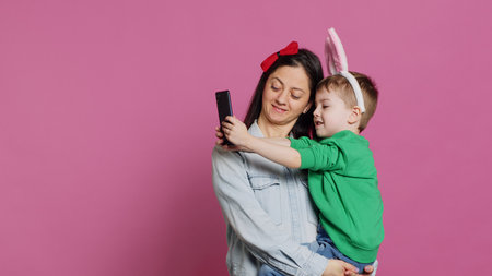 Lovely small child taking pictures with his mother on smartphone, trying to capture fun and cute moments against pink background. Little boy being playful and fooling around with phone. Camera A.の写真素材