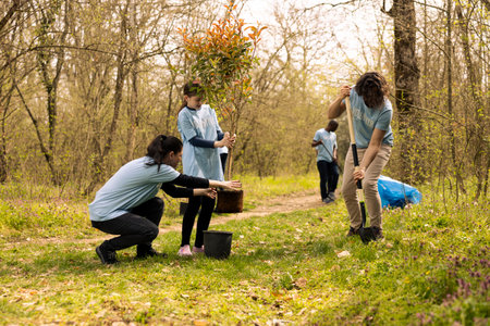 Team of activists planting trees around the woods area for nature preservation, doing voluntary work for a conservation project. Environmental enthusiasts plant seedlings together.の写真素材