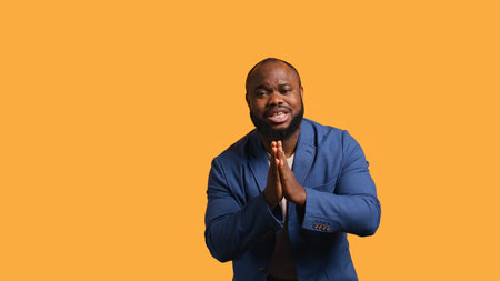 African american man putting hands together in begging gesture, making wish, isolated over yellow studio background. BIPOC person asking for something, praying and hoping, camera Bの写真素材