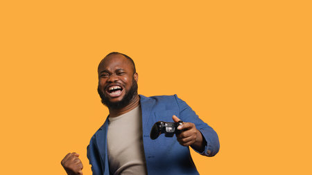 Joyous BIPOC gamer celebrating after winning gaming console game, studio background. Delighted man bragging after being victorious in videogame, defeating all enemies using gamepad, camera Aの写真素材