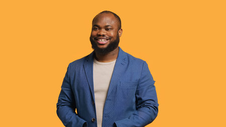 Portrait of cheerful african american man smiling, looking pleased, isolated over yellow studio background. Happy expressive BIPOC person stylishly dressed grinning, feeling satisfied, camera Aの写真素材