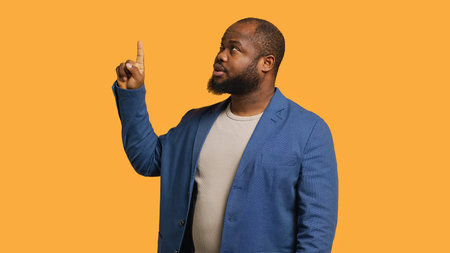 Salesman pointing upwards with finger doing recommendation, talking with audience. BIPOC person looking up, showing copy text, isolated over studio background, camera Aの写真素材