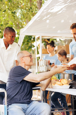 Charitable team offers help to the destitute and distributes free food including fresh fruits to homeless. A wheelchair-bound disabled individual also receives hunger alleviation assistance.の写真素材