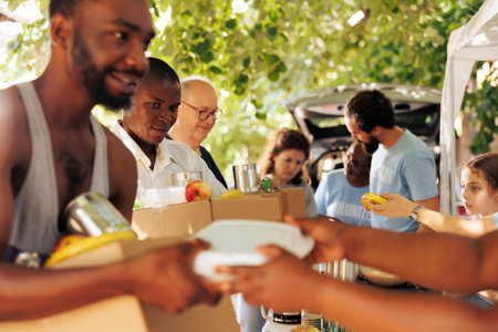 Multiethnic group of volunteers providing humanitarian aid to homeless people. They distribute meal boxes canned goods and packages with genuine smiles helping to alleviate poverty and hunger.の写真素材