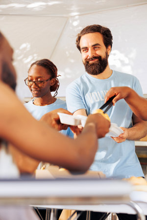 Portrait of a friendly volunteer distributing free food to a crippled homeless person. Detailed image shows a caucasian man helping during a food drive to serve hot meals to the poor and needy.の写真素材