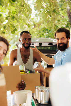 Less fortunate african american man receives canned goods and donation box from caucasian male volunteer. Image showcasing charitable effort aimed to alleviate poverty and hunger within the community.の写真素材