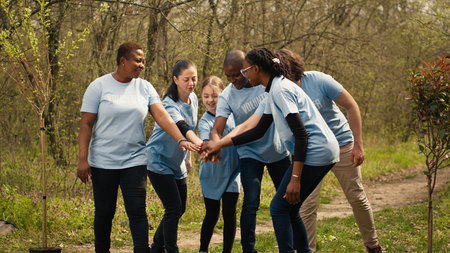 Cheerful proud team of activists join forces to clean a forest, celebrating their volunteering work by connecting hands together. Happy people showing responsibility for the environment. Camera A.の写真素材