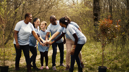 Cheerful proud team of activists join forces to clean a forest, celebrating their volunteering work by connecting hands together. Happy people showing responsibility for the environment. Camera B.の写真素材