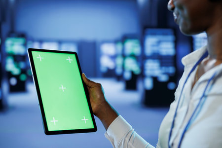 Experienced developer in server room uses green screen tablet to future proof network from downtimes and unexpected system failures. IT specialist with mockup device ensures increased data securityの写真素材