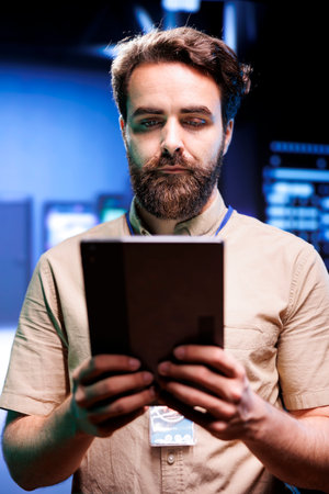 Vertical portrait of serviceman in server farm with supercomputers used for computationally intensive tasks such as scientific simulations. Employee doing annual equipment checkup using tabletの写真素材