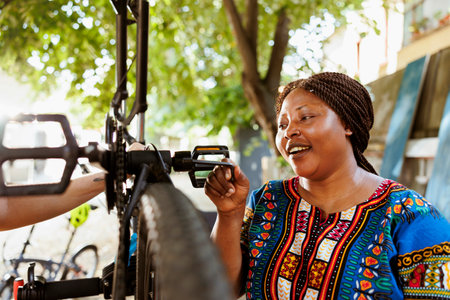 Vibrant sporty african american female fixes bicycle components with professional work tool from home yard. Active enthusiastic black woman outdoors using allen key to repair bike crank arm and pedal.の写真素材