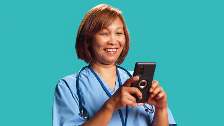 Jubilant nurse having burst of joy at work while chatting with friends, isolated over studio background. Elated hospital worker delighted about great news she received over the phone, close upの写真素材