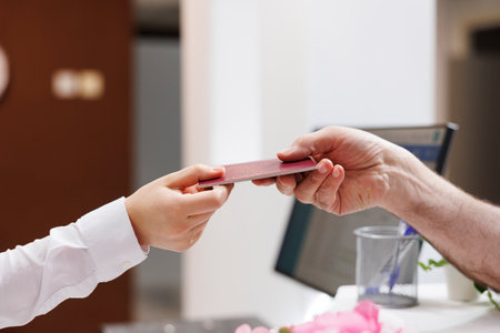 Close-up shot of caucasian pair of hands grasping passport for check-in verification procedure. In hotel reception, senior man handing his personal document to concierge for reservation.の写真素材