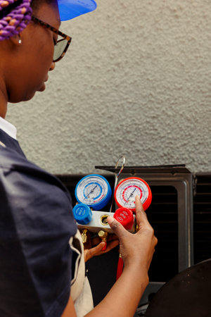Capable specialist comissioned by customer to restore cooling capacity of air conditioner by inspecting system for leaks and recharging it with new refrigerant to prevent compressor issuesの写真素材