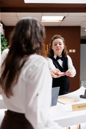 At hotel lobby counter, elderly female traveler checks in with passport. After establishing identity, kind concierge at registration counter returns the personal paperwork of retired senior woman.の写真素材