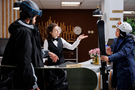 In hotel lobby, young couple interacts with helpful staff for check-in, reservations and assistance. Visitors in winter gear prepare for a ski holiday, capturing the excitement of a winter getaway.の写真素材