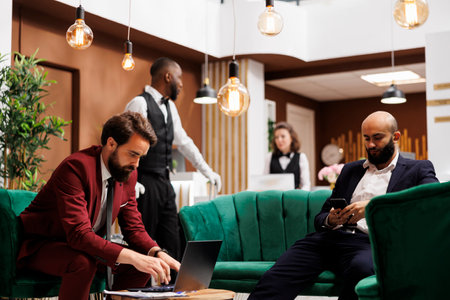 Two businessmen working in lounge area, elegant hotel atmosphere with important guests wearing suits. Entrepreneurs preparing for speech at international official conference.の写真素材